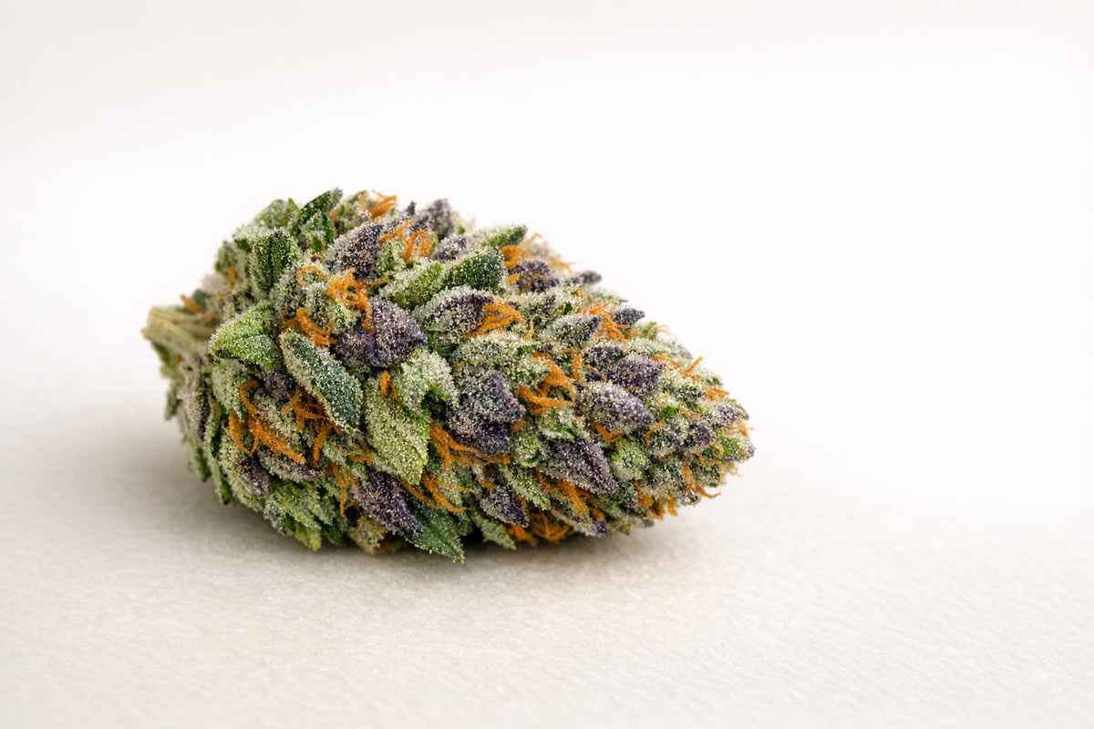 Close-up of a premium cannabis flower bud with purple hues and orange hairs on a white background